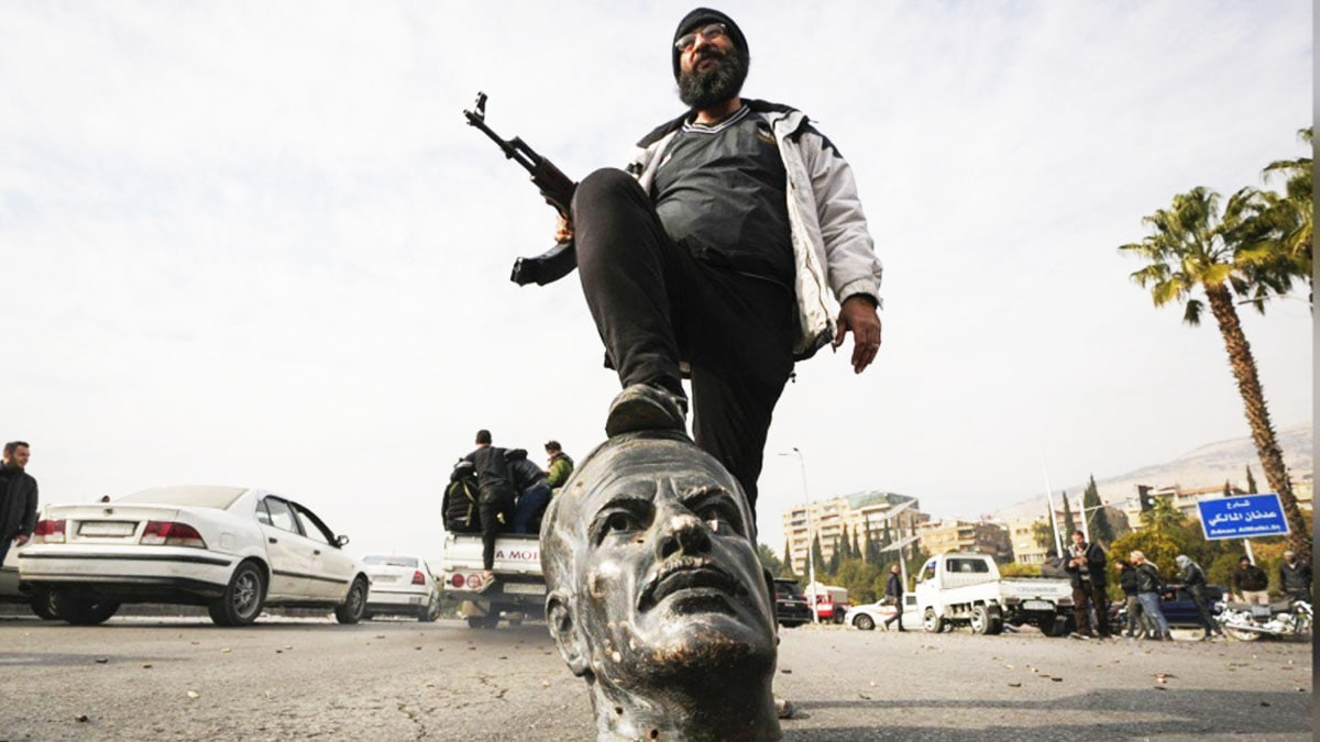 Rebels celebrate by stepping on a statue of Bashar's father, AK-47s in hand